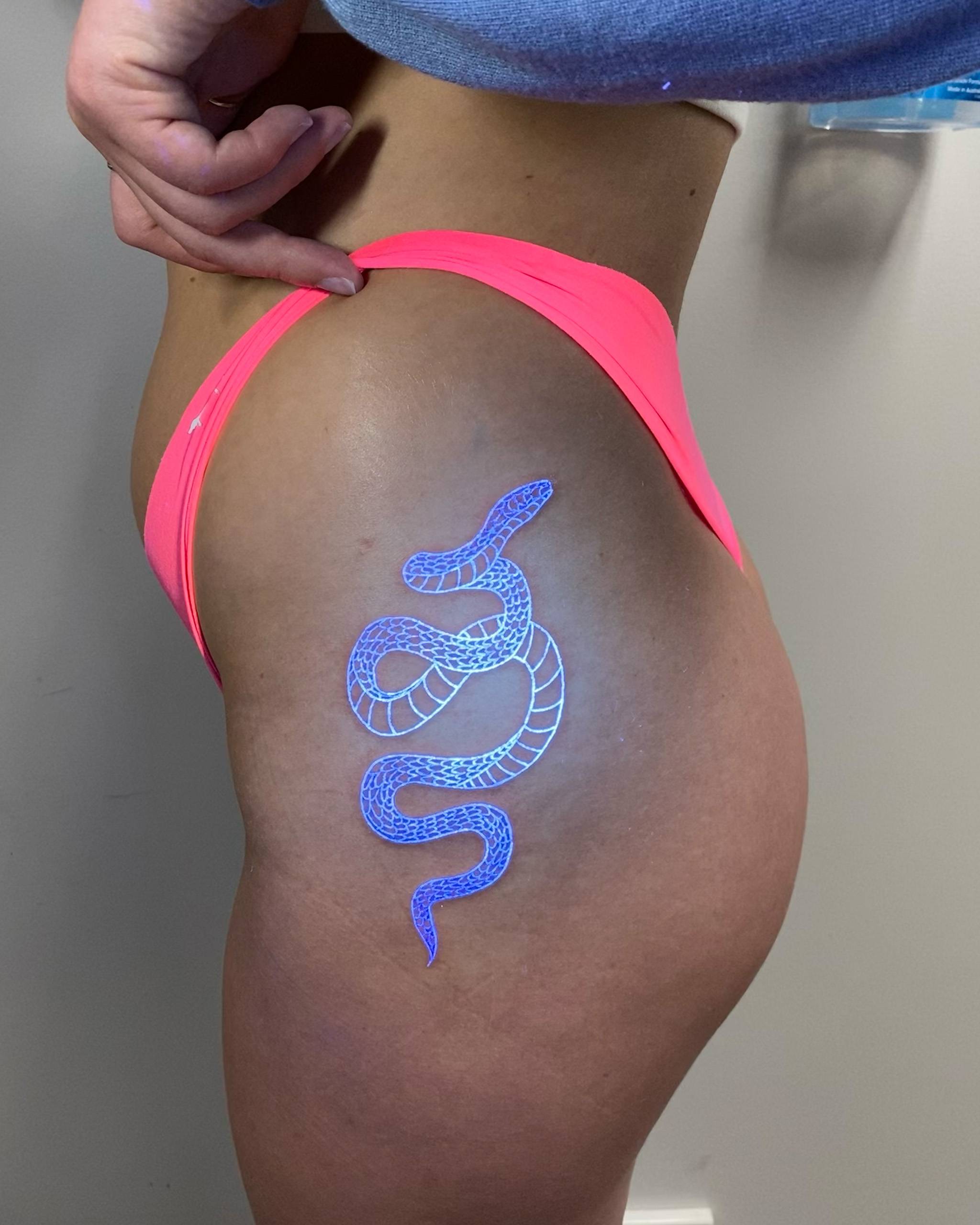 Blue UV-reactive snake tattoo design on hip