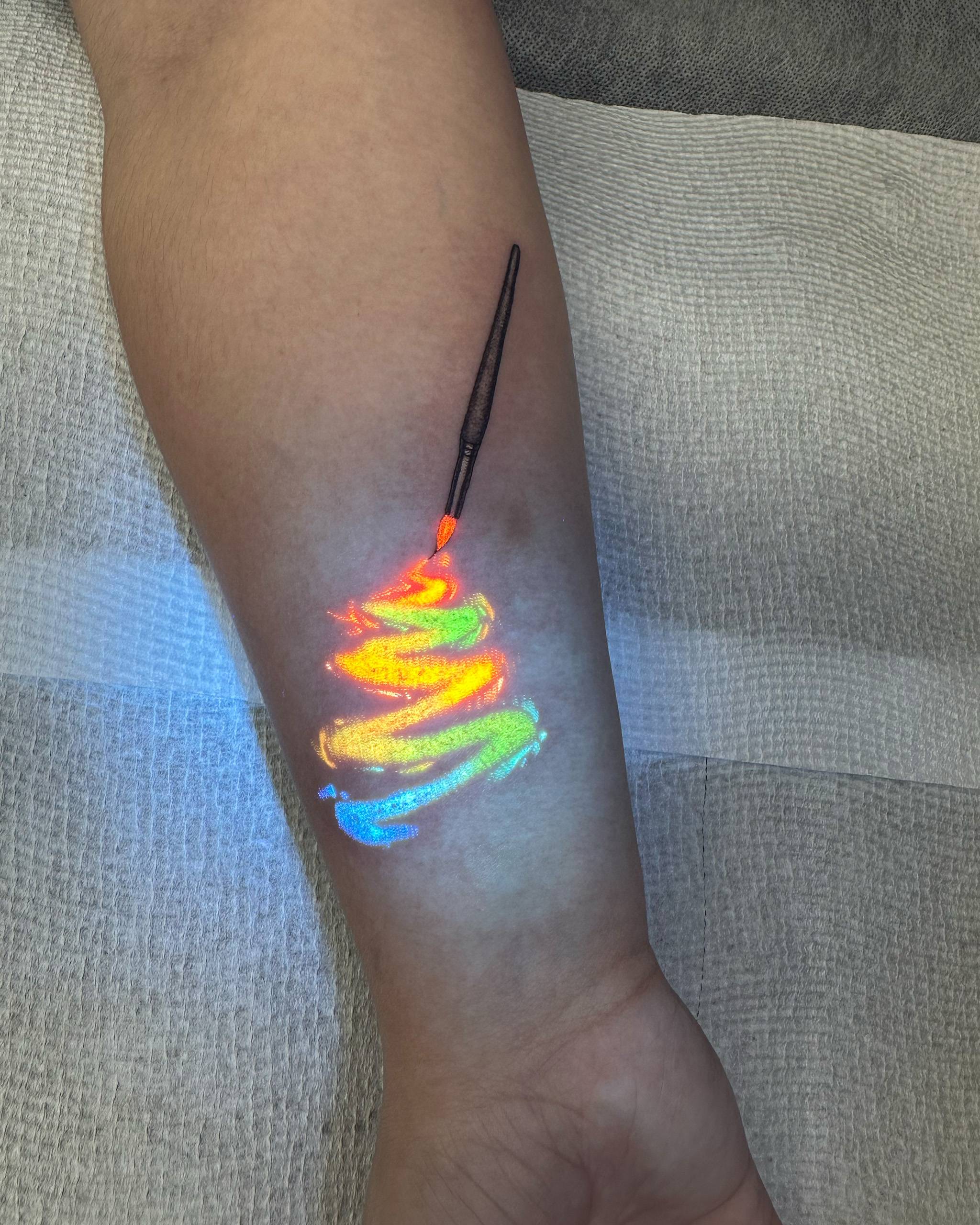 Artistic paintbrush with rainbow UV-reactive paint stroke tattoo