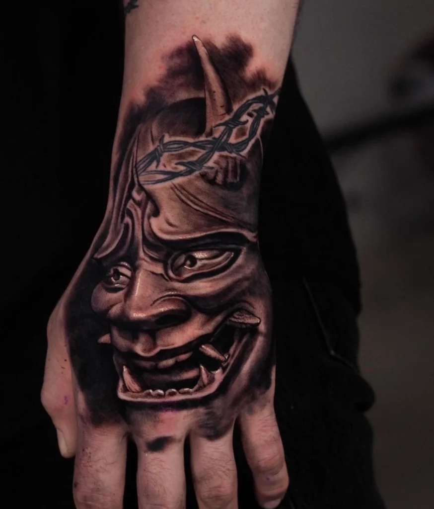 A striking black and gray tattoo of a Hanya mask covering the hand, showcasing Dylan's expertise in combining traditional Japanese art with realism