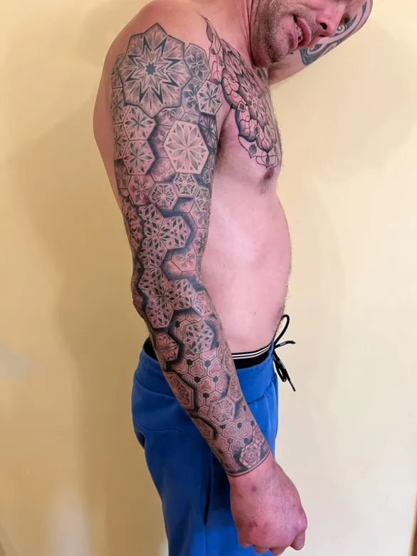 Chest tattoo with colored lilies framing hexagonal geometric pattern centerpiece