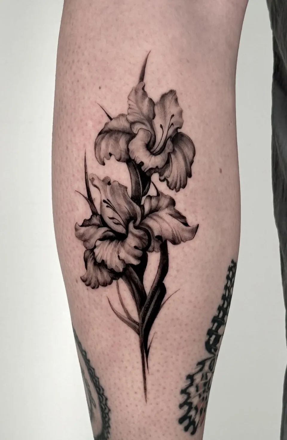 Detailed floral tattoo with realistic lily flowers in black and grey